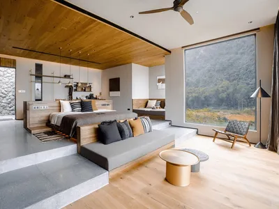 A modern minimalist bedroom with a large window overlooking a natural landscape, featuring a bed with black and white pillows