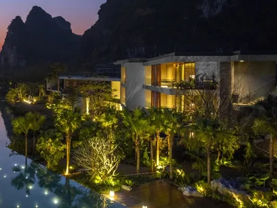 Modern resort hotel with concrete architecture, illuminated poolside area, and palm trees at dusk