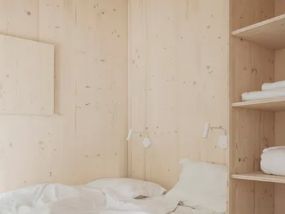 A minimalist bedroom with white wood walls and a bed with white bedding.