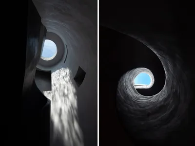 A circular, concrete staircase with a central skylight, leading upwards in a spiral pattern.