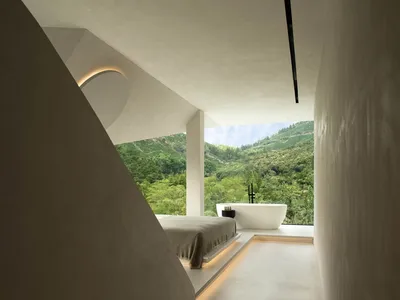 Modern minimalist bedroom featuring a concrete bed platform and bathtub, with a view of lush greenery outside.