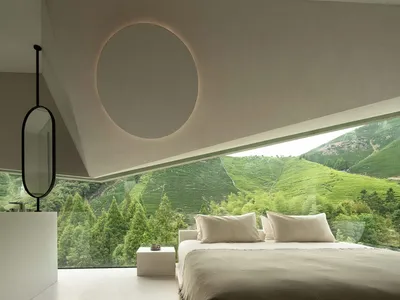 Minimalist bedroom with concrete floor, glass windows, and green landscape view.