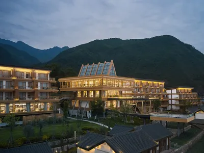 A modern resort with wooden frame and glass features, set against a mountainous backdrop.