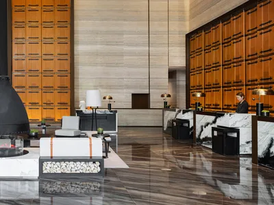 A modern hotel lobby featuring marble and concrete finishes, with a receptionist desk and seating area.