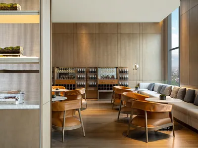 A modern restaurant bar with wooden flooring, leather chairs, and metal shelves.