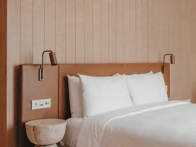 Minimalist bedroom with wooden walls, white bedding, and textured side table.