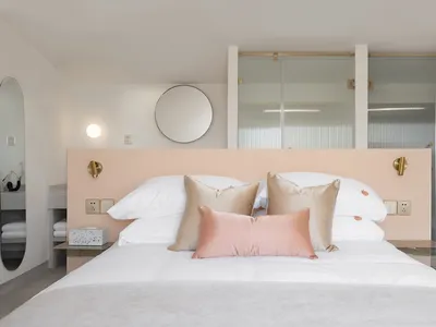 A minimalist bedroom with a white cotton mattress on a bed with a peach-colored bed frame, white cotton pillows, and peach-co