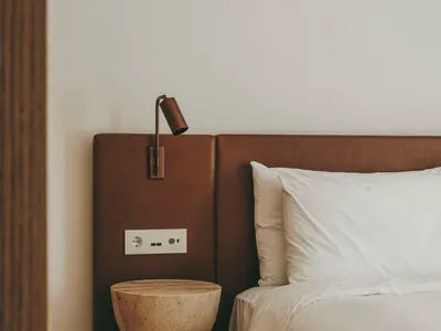 Modern minimalist bedroom featuring a bed with a brown leather headboard, white bedding, and a natural stone side table with