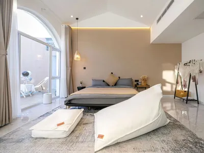 A minimalist bedroom featuring a bed with white pillows on a white floor, with a white arched window and a white arched rug.