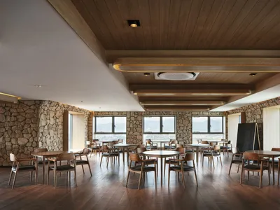 A spacious, modern restaurant cafe with round tables, wooden chairs, and stone walls, featuring a warm and inviting atmospher