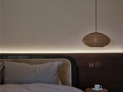 A minimalist bedroom with a woven wicker pendant light and a bed adorned with grey pillows and blanket, set against a plain w