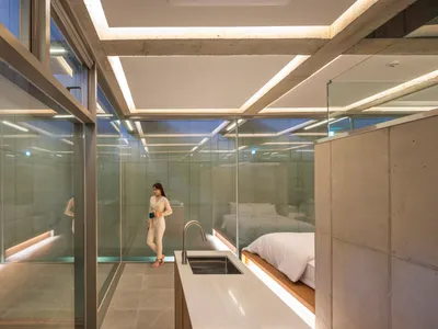 Modern minimalist bedroom with concrete walls, glass walls, and a white bed.