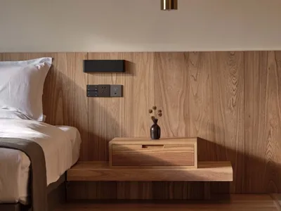 A minimalist bedroom featuring a wooden bed, wooden headboard, and wooden floating nightstand with a vase and a lamp hanging