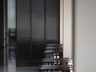 A row of wooden dining chairs arranged in a restaurant interior. The chairs have a minimalist design and are set against a sl