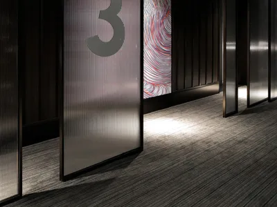 A modern hotel corridor with glass dividing panels and ceiling lighting.