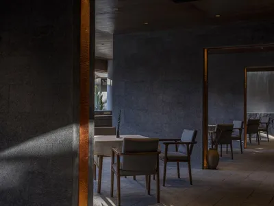 A modern restaurant interior with concrete walls, minimalist furniture, and industrial lighting.