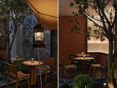 Industrially designed restaurant seating area with wooden tables and chairs, a lantern, and greenery.