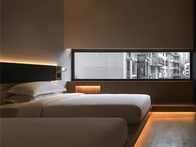 A minimalist hotel room with a small window, wooden flooring, and glass walls.