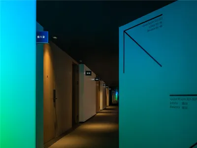 A modern hotel hallway illuminated with warm lighting, featuring room signs and directional arrows.