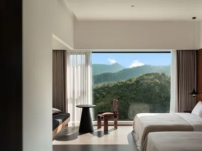 Modern, minimalist bedroom with wooden furniture and a scenic view of mountains through a large window.