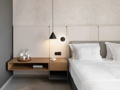 A minimalist hotel room features a concrete floor, white linens, and simple furnishings.