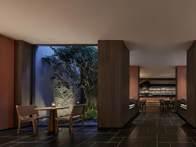 A modern restaurant interior with dark tones, wooden tables, chairs, and stone walls.