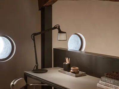 A modern, industrial home office featuring a concrete desk, metal lamp, and round windows.