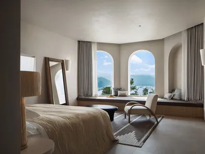 A contemporary bedroom featuring sleek furniture, a comfortable fabric bed, and a cozy seating area with a view of the water.