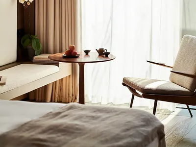 A modern minimalist bedroom featuring textured fabric upholstery, a small round table with a teapot and apples, and natural l