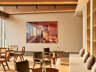 Modern restaurant bar interior with wooden furniture, tables, and chairs, featuring a large framed photograph on the wall.