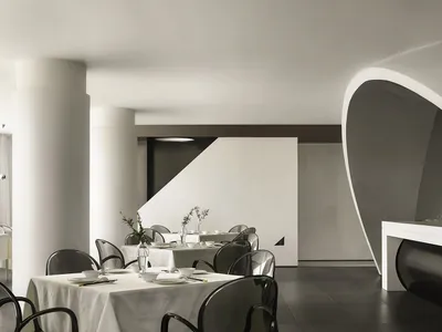 Interior of a modern restaurant with concrete walls and floors, white tables and chairs, and minimalist design.