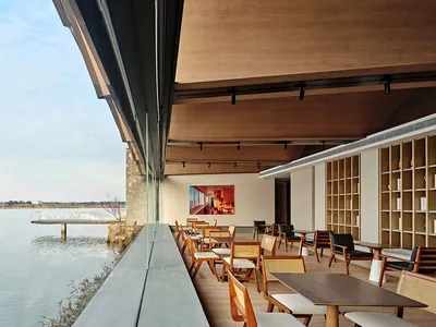Modern restaurant interior with glass walls overlooking a serene waterfront.