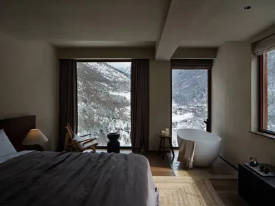 一間現代臥室，鋪設地毯地板，搭配極簡家具，並透過大窗欣賞雪山景色。