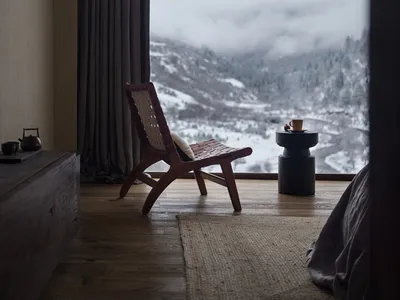 A bedroom with a mountain view, featuring a wooden chair and a side table with a cup and saucer.