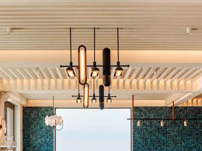 Modern restaurant interior featuring wooden tables, glass chandeliers, and blue-tiled walls with a view of the ocean.