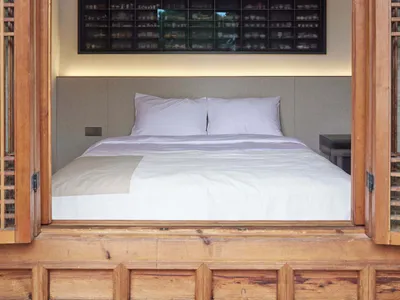 A minimalist bedroom with a bed nestled within a wooden box, featuring a display case filled with ceramics on the wall.