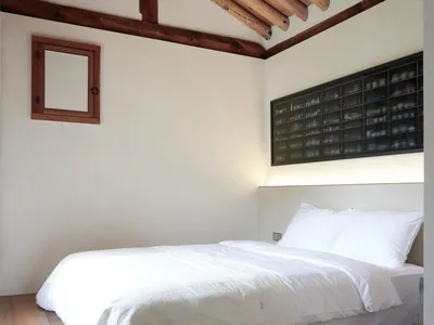 Modern minimalist bedroom with wood furnishings, white bedding, and a wooden ceiling with exposed beams.