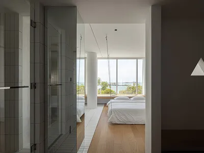 Bedroom with white tiled walls and hardwood floors, featuring a white bed with white bedding, large windows overlooking the s