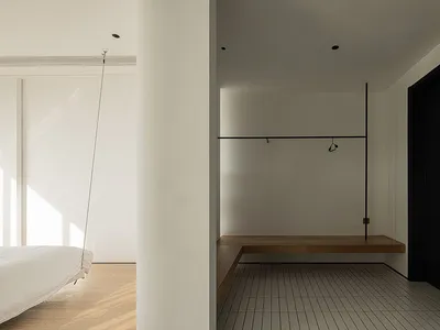 A minimalist bedroom featuring a floating bed, white walls, and a wooden floating bench.