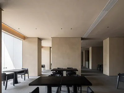 A minimalistic restaurant interior featuring concrete walls and metal tables and chairs.