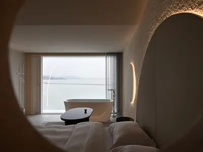 A modern bedroom featuring a concrete floor, glass walls, and minimalist decor.