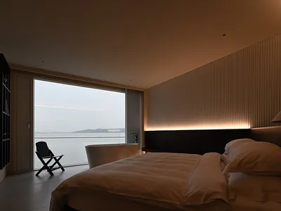 現代極簡臥室，擁有大型窗戶俯瞰水景，搭配質感畫布牆面與柔和暖光。
