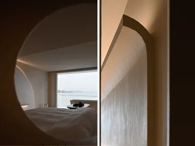 A modern minimalist bedroom featuring concrete walls and a view of the ocean through a large window.