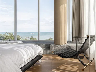 A modern minimalist bedroom with a glass wall overlooking the ocean.
