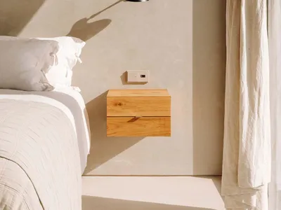 Minimalist bedroom with a wooden floating nightstand, window with curtains, and soft lighting from a wall-mounted sconce.