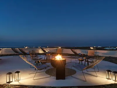 Industrial-style outdoor lounge with metal chairs and a fire pit at night.