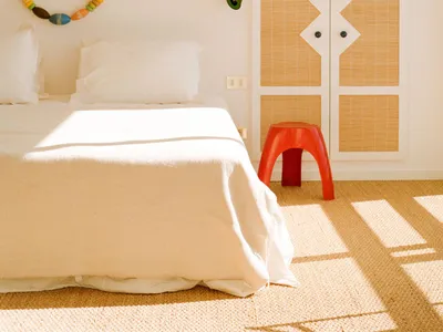 A minimalist bedroom with a bed covered in a white sheet and pillows, adorned with a colorful beaded garland hanging on the w