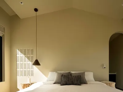 Modern minimalist bedroom featuring a bed with a white duvet and neutral-colored accent pillows, set against a beige wall and