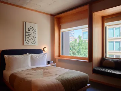 A minimalist bedroom with a wooden bed frame, white bedding, and a wall-mounted light fixture.