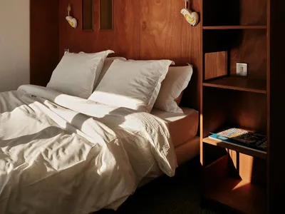 A minimalist bedroom featuring a wooden bookshelf with built-in lighting and storage.
